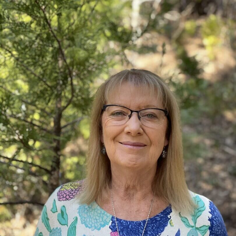 A woman with glasses standing in front of trees.